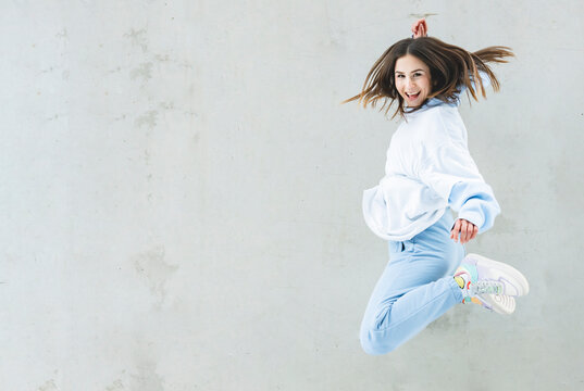 Happy woman smiling while jumping against gray wall