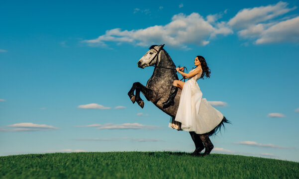 Bride in white dress sits horseback on rearing horse.