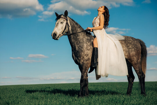 Bride in white dress sits horseback on dapple grey horse.