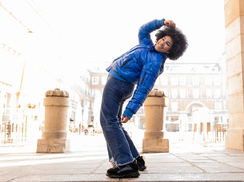 Smiling woman bending backwards while standing on footpath