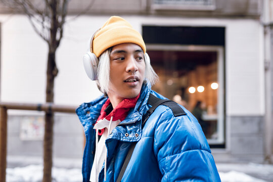Young man listening music while looking over shoulder during winter