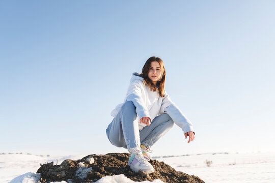 Young woman staring while crouching on rock against sky