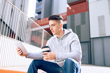 Young man holding reusable coffee cup while using digital tablet against building