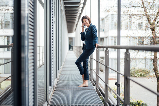 Smiling female entrepreneur talking on smart phone against railing in balcony