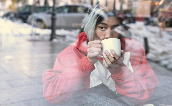 Asian man drinking coffee seen through glass in cafe during winter