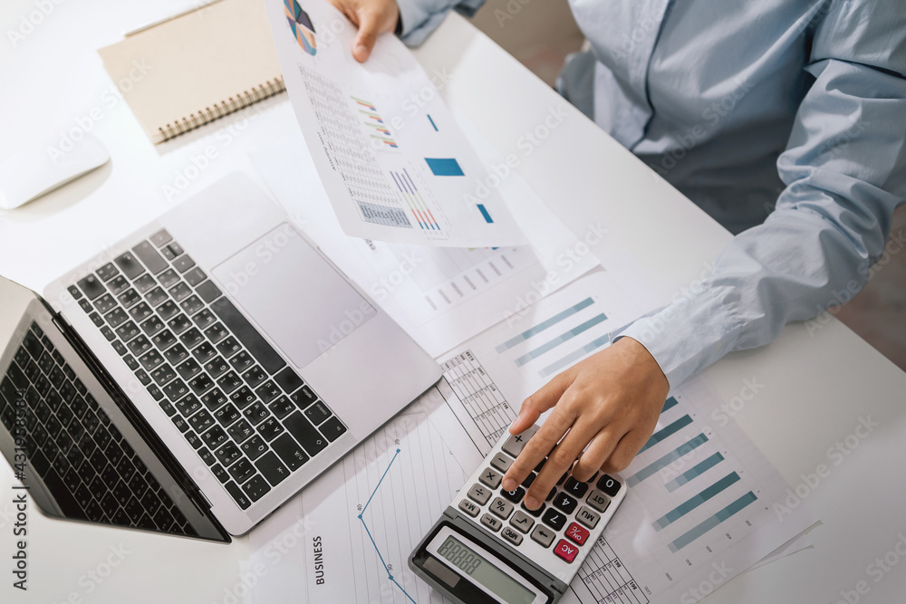 Wall mural Woman accountant use calculator and computer with holding pen on desk in office. finance and accounting concept