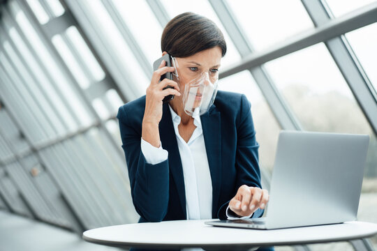 Mature businesswoman talking on smart phone while working in office during COVID-19