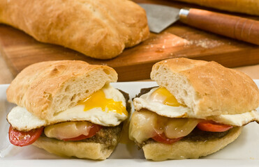 front view, close distance of a fried egg and sausage sandwich  with cheese, tomato and lettuce, cut in half