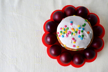 Traditional Easter cake with decorative glaze. Orthodox food after fasting on the Easter holiday. Red-painted chicken eggs on a stand on a light tablecloth