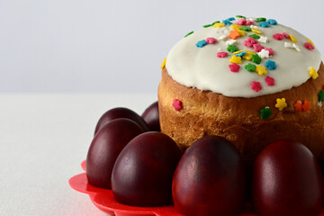 Traditional Easter cake with decorative glaze. Orthodox food after fasting on the Easter holiday. Red-painted chicken eggs on a stand on a light tablecloth