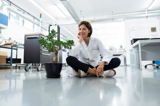 Female engineer with hand on chin sitting on floor in industry