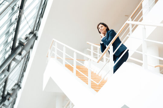 Thoughtful businesswoman with hand on chin leaning over railing in corridor