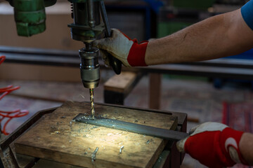 metal worker drilling holes in metal with a bench drill