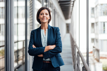 Smiling confident businesswoman with arms crossed standing on balcony