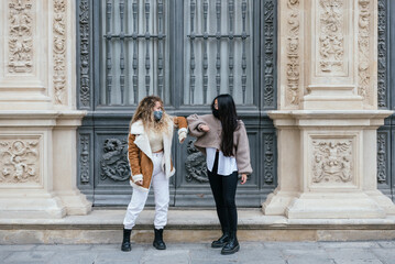 Multi-ethnic female friends giving elbow bump wearing protective face mask during pandemic
