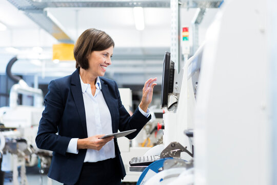 Happy businesswoman with digital tablet operating machinery in factory