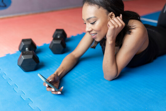 Smiling Young Woman Using Mobile Phone While Lying In Gym