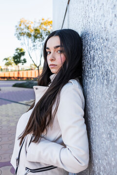 Teenage girl with hand in pocket while leaning on silver wall