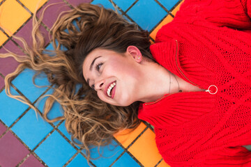 Smiling woman looking away while lying down on tiled floor