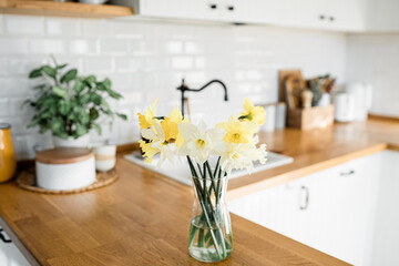 Fototapeta na wymiar daffodils bouquet in vase on the table white kitchen view
