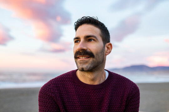 Handsome man in maroon sweater day dreaming at beach during sunrise - Powered by Adobe