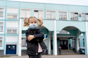 little blonde cute girl near school wearing a mask, covid-19 prevention concept