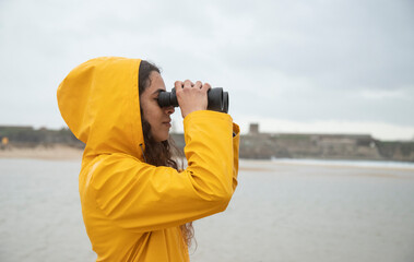 Young woman looking through binoculars while standing at beach