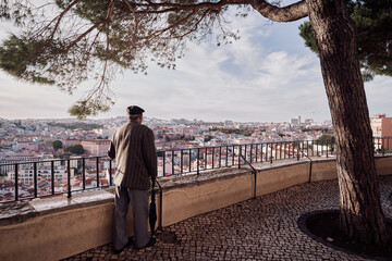 Old man enjoying Lisbon city view, red tiled roofs and ancient architecture. - obrazy, fototapety, plakaty