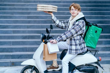 Foto op Plexiglas Outdoor portrait of delivery service man holds pile of boxes with tasty pizza, reaches destination fast on motorcycle, has friendly outlook, brings order for customer. Food transporting concept. © Iryna