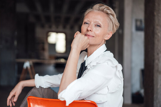 Blond businesswoman with hand on chin sitting on chair on loft apartment