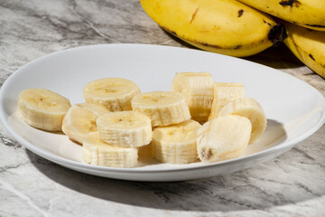 A bunch of bananas and a sliced banana on a plate on a table