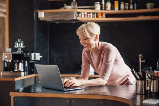 Happy Businesswoman Working On Laptop At Kitchen Counter In Home Office