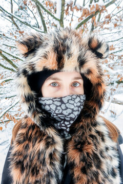 Mature woman wearing leopard print fur hat staring while standing against tree during winter