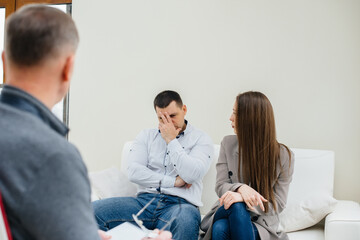 Fototapeta na wymiar A young married couple of men and women talk to a psychologist at a therapy session. Psychology.