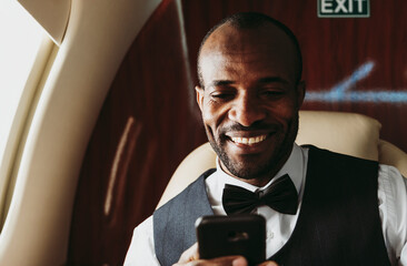 Smiling businessman text messaging on smart phone in private jet