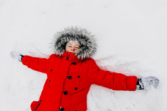 Girl in red warm clothing making snow angle during winter