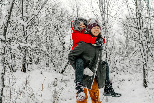 Teenage girl giving piggyback to sister against snow covered bare trees in forest