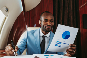 Smiling businessman analyzing graph in private jet