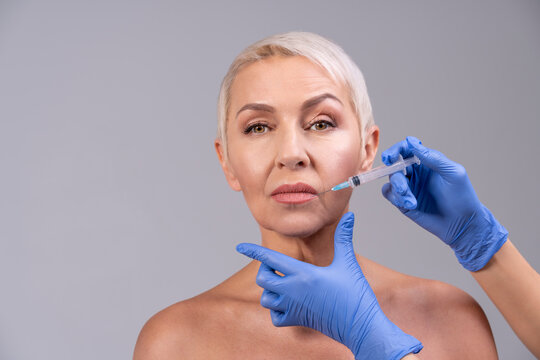 Doctor injecting senior woman lip while standing against gray background