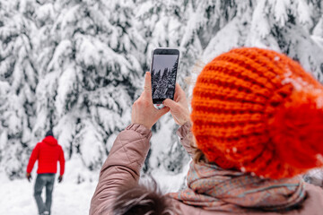 Mature woman taking photo of tree through mobile phone while standing with man in background at forest