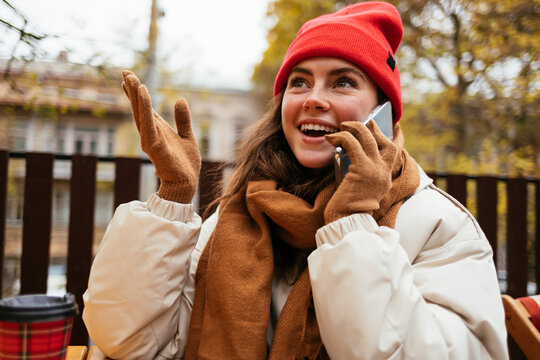 Smiling woman wearing knit hat gesturing while sitting at sidewalk cafe
