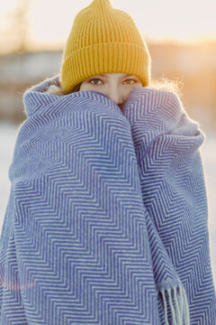 Portrait of beautiful girl wearing knit hat warming herself up with wool blanket
