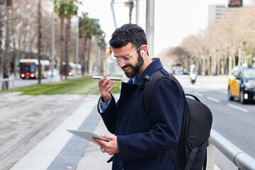 Smiling businessman with digital tablet talking on smart phone through speaker at station