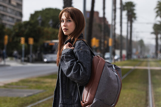 Redhead woman with backpack at tram station looking away