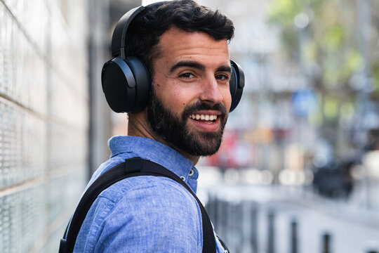 Smiling young businessman listening music through wireless headphones