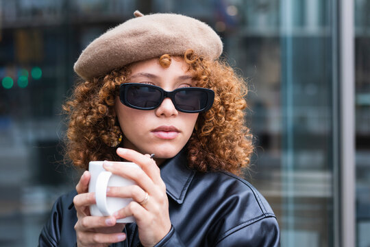 Female teenager wearing beret and sunglasses having coffee outdoors