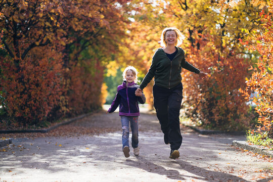 Happy mother and daughter holding hands and running in park during autumn