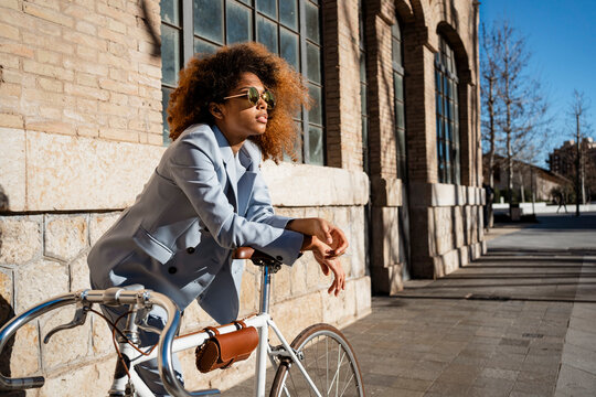Afro woman in sunglasses leaning on bicycle against building