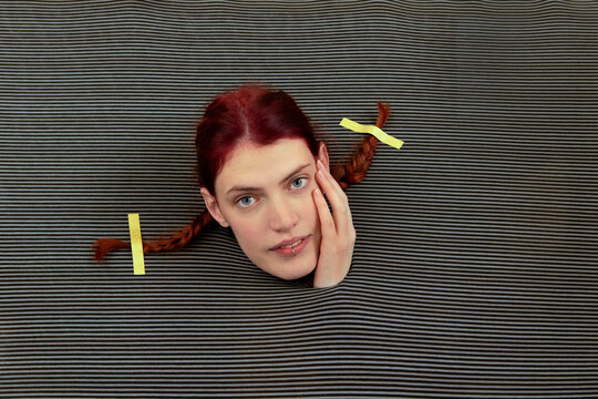 Studio shot of head of young woman wearing pigtails sticking out of gray striped background