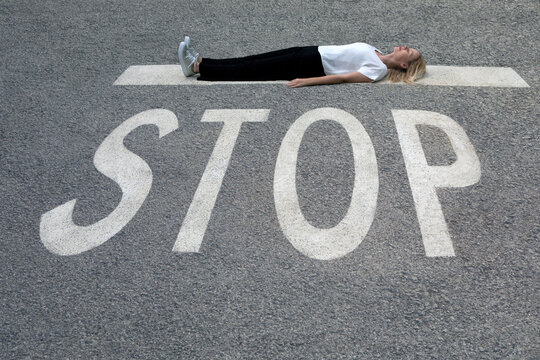Woman in casual clothing lying on road at STOP sign